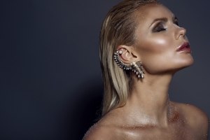 Portrait of chic gorgeous blond woman with wet hair, artistic glittering make-up and the cuff on her ear posing with closed eyes. Isolated on grey background. Copy-space. Jewellery concept. Close up